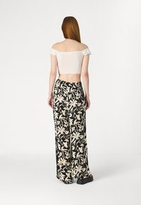 White off-the-shoulder crop top with ruffled sleeves paired with black wide-leg pants featuring a beige floral pattern.