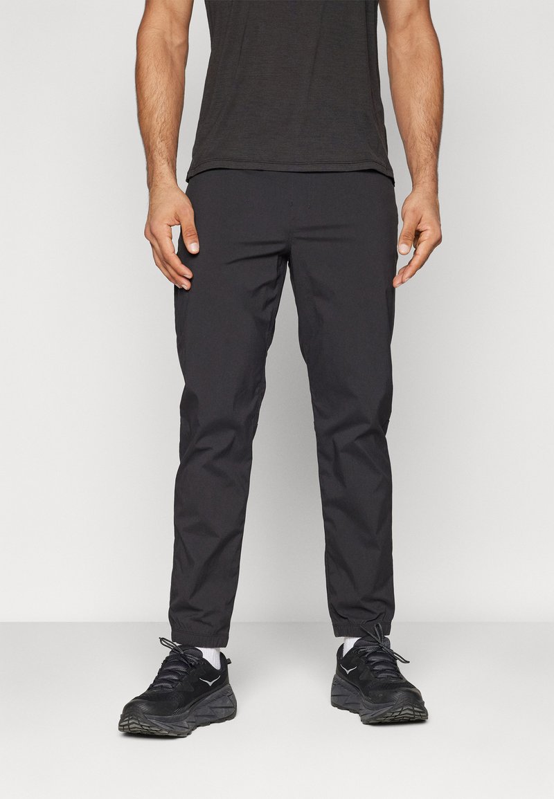 Herre slim-fit ankel-lange svarte bukser, laget av lett materiale med en glatt tekstur, kombinert med svarte treningssko.