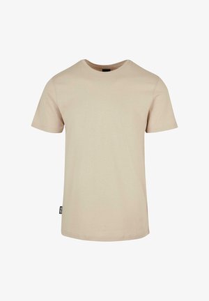 Beżowy t-shirt z krótkim rękawem i okrągłym dekoltem, z małą czarną metką na lewym szwie bocznym na jednolitym białym tle.