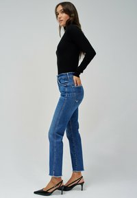 Top negro de manga larga combinado con jeans azules de tiro alto. Los jeans tienen un corte recto y un dobladillo deshilachado. Los tacones negros de punta acentúan el look.