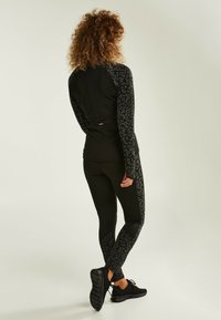 Svart träningskläder med leopardsmönstrade detaljer på ärmar och sidor, med en åtsittande design och textilmaterial. Utmärker sig för sin eleganta silhuett.