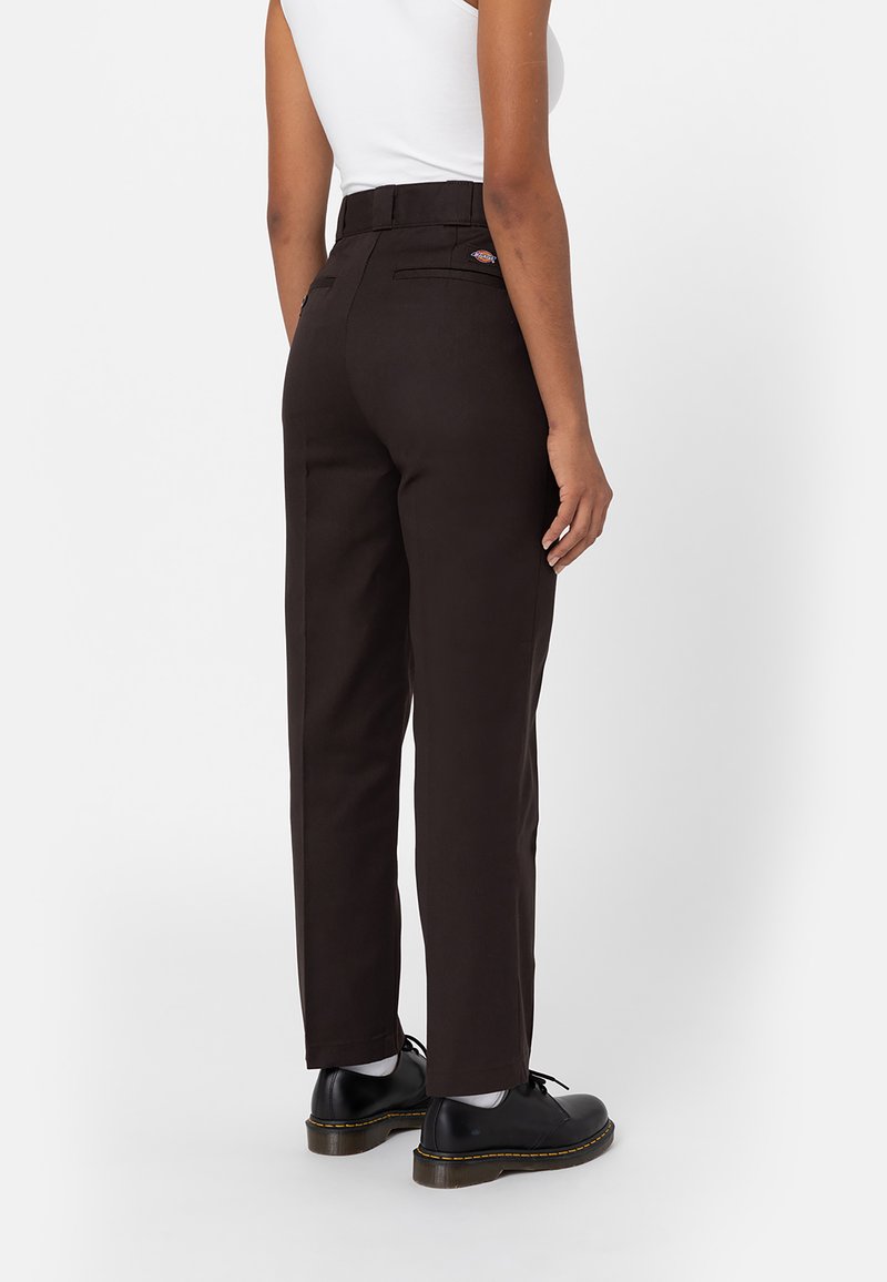 Pantalones rectos marrones hechos de algodón con una textura suave. Presentan dos bolsillos traseros y un lazo para cinturón. Llevados con zapatos negros.
