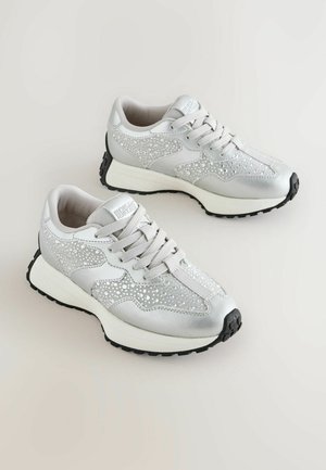 Graue Sportschuhe mit funkelnden Strassakzenten, Netzpaneelen und einer schwarzen Gummisohle. Die Schnürsenkel sind hellgrau und verfügen über ein gepolstertes Design.