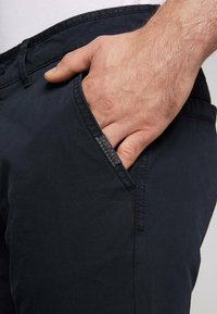 Pantaloni blu navy realizzati in tessuto tessuto, con una tasca laterale e cuciture a vista. Un'etichetta è visibile vicino all'apertura della tasca.