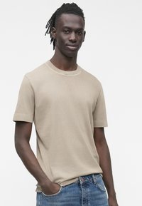 Béžové tričko s krátkým rukávem z bavlny, s kulatým výstřihem a volnějším střihem. Nošeno s modrými džínami, které vytvářejí ležérní vzhled.