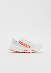 White athletic shoe with orange "TERREX" branding, textured upper, padded collar, and white midsole with orange accents on the outsole.