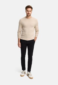 Maglione beige a maglia lavorata con maniche lunghe, abbinato a pantaloni neri slim-fit e sneakers bianche con dettagli beige.