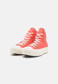 Zapatillas altas de color coral con cordones blancos, puntera de goma y suela de plataforma blanca texturizada. Parte superior de lona con ojetes de metal para los cordones.