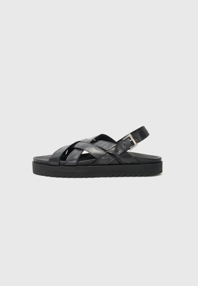 Sandali in pelle nera con design a tracolla incrociata, fibbia regolabile e una suola nera comoda con superficie texture.