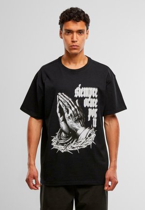 Nuori mies, joka on pukeutunut mustaan T-paitaan, jossa on rukouskädet, thornikruunu ja valkoisella tekstillä "siempre ore por ti" edessä.