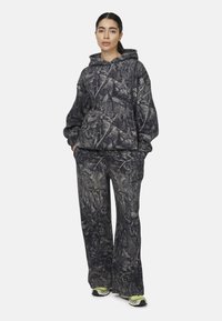 Camo-gepatroneerde hoodie en bijpassende broek in grijstinten en zwart. Zachte stof met een relaxed fit en elastische manchetten.