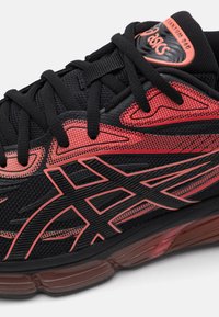 Black athletic shoe with red accents, mesh upper, textured patterns, and sturdy laces. Features a thick, cushioned sole for support.