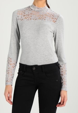 Graues Langarmoberteil mit einer Spitzenpartie über der Brust und Spitzenakzenten an den Ärmeln. Glatte Textur, hoher Halsausschnitt, figurbetontes Design.