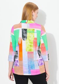 Camisa de tres cuartos colorida con patrones abstractos en verde, rosa, naranja y negro, con una tela suave y un corte relajado.