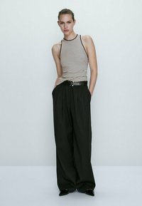 Stribet tanktop med sort kant parret med højtaljede, løse sorte bukser. Modellen bærer et sort bælte og spidse sorte sko.