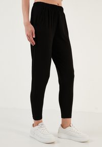 Zwarte joggerbroeken met elastische taille en taps toelopende pijpen, zijzakken en een soepele textuur, gecombineerd met witte sportschoenen.