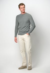 Ljusgrå, åtsittande tröja med ribbad halsringning, i kombination med krämfärgade raka byxor och beige sneakers, mot en enfärgad bakgrund.