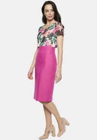 Kwiatowa bluzka z krótkim rękawem w wielokolorowym wzorze, połączona z dopasowaną różową spódnicą ołówkową. Modelka nosi nude szpilki.