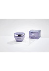 Lavender Kérastase Paris Haarmaske Behälter mit silbernem Deckel neben passender verpackter Verpackung auf klarer Acrylplattform.
