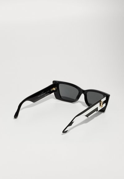 Black sunglasses with angular frame, dark lenses, and contrasting white stripes on arms. Features gold-toned hardware on temples.