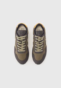 Pantofi sport verzi și gri din materiale din plasă și piele întoarsă. Prezintă șireturi rotunde, tălpi din cauciuc și un accent vibrant galben la călcâi.