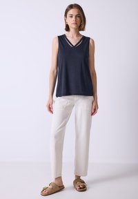 Top senza maniche blu navy con scollo a V e doppie spalline, abbinato a pantaloni bianchi a sigaretta e sandali beige senza chiusura.
