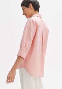 Camicia col collare rosa chiaro con maniche a tre quarti, polsini arricciati e design a orlo curvo; realizzata in un tessuto morbido e leggero.