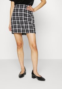 Svart och vit rutigt kjol med en något utfläkt design, mitt på låret längd och franskanter, tillsammans med svarta klackskor med platt block.