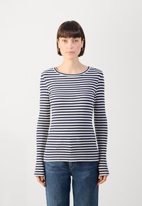 Gestreifte Langarmbluse aus nachtblauem und cremefarbenem Rippstoff, mit rundem Ausschnitt und taillierter Silhouette, kombiniert mit blauen Jeans.