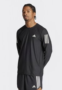 Černé atletické tričko s dlouhým rukávem z lehké látky, s bílými třemi pruhy na obou rukávech a malým logem na hrudi.