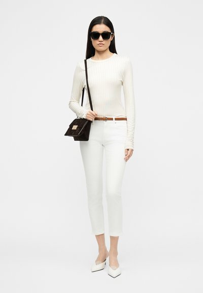 Γυναίκα με μαύρα γυαλιά ηλίου, λευκό ριμπ μπλουζάκι με μακριά μανίκια, λευκό κοντό παντελόνι, λευκά μυτερά ψηλοτάκουνα, καφέ ζώνη και μαύρη τσάντα χιαστί.