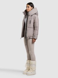 Vatteret jakke i lys beige med høj krave, lynlåslommer og elastiske ærmegab, kombineret med cremefarvede snestøvler og tætsiddende leggings.