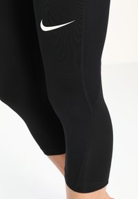 Czarne legginsy sportowe wykonane z elastycznego materiału o gładkiej teksturze. Posiadają białe logo Nike oraz długość do kolan.