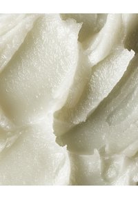 Produit cosmétique blanc crémeux avec une texture lisse et réfléchissante, présentant des pics et des plis doux et superposés qui mettent en valeur sa consistance épaisse.