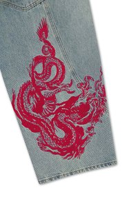 Light blue denim fabric featuring a large, detailed red embroidered dragon design near a seam and stitched pocket.