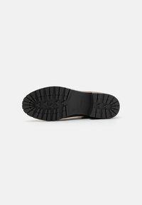 Semelle de chaussure en caoutchouc noir avec un motif de semelle profond, une surface texturée et un logo rectangulaire sur le côté pour une meilleure adhérence et durabilité.