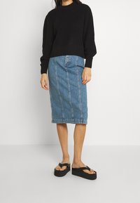 Svart ribbad tröja, ljusblå denimpennkjol med synliga sömmar och svarta plattformssandaler.