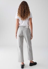 Pantaloni larghi grigio chiaro realizzati in cotone morbido, caratterizzati da una vita alta, tasche posteriori e un design senza cuciture. Abbinati a scarpe nere basse.