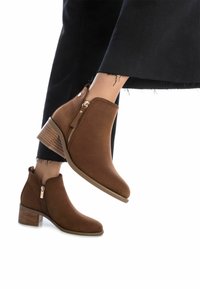 Stivaletti in camoscio marrone con punta affilata, detail con zip laterale e tacco impilato, abbinati a jeans scuri con orli sfilacciati.