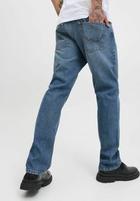 Ljusblå denimjeans med avslappnad passform, femficksdesign, synliga sömnadsdetaljer och i kombination med svarta skor.