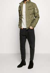 Olivgrön, lätt jacka med flera fickor och hög krage. Matchad med mörka jeans och svarta chelseaboots.