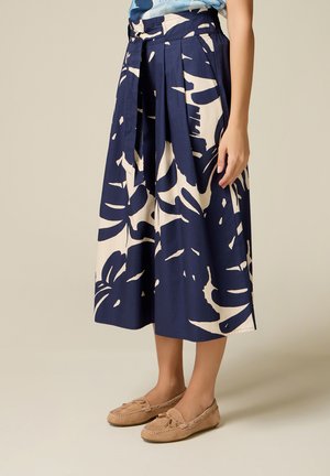 Pantalones culotte azul marino de pierna ancha con estampado abstraco de hojas blancas, cinturón atado en la cintura, combinados con mocasines beige.