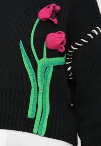 O suéter de malha preto apresenta caules de tulipas bordados em verde com flores pink. Os destaques incluem um design texturizado e detalhes de costura.