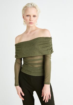 Olivgrön off-shoulder topp med rynkad textur, genomskinliga långa ärmar och en figurnära design, matchad med mörka, ribbade byxor.