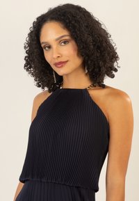 Vestido de color marino con plisados y escote halter, que presenta un detalle de hardware dorado en el cuello. Textura suave con una silueta fluida.