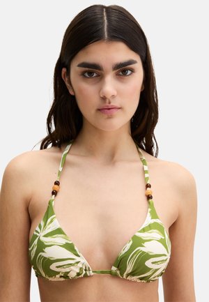 Joven mujer de cabello oscuro que lleva un top de bikini verde y blanco con estampado de hojas y detalles de cuentas de madera en las tiras.