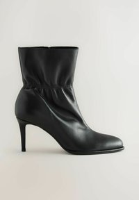 Must musta kõrge kontsaga kreeniga must nahkne põlve keskmise kõrgusega saabas, millel on terav varvas ja kerge rütmi paindumine pahkluu ümber.