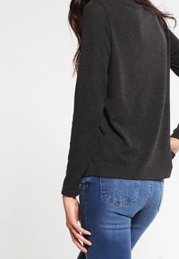 Czarna bluzka z długim rękawem wykonana z miękkiego materiału, o luźnym kroju i okrągłym dekolcie, zestawiona z niebieskimi obcisłymi dżinsami.