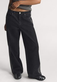 Čierne džíny s širokými nohavicami a vysokým pásom, s piatimi vreckami a bielymi bočnými pruhmi. Vyrobené z denimu s hladkou textúrou.