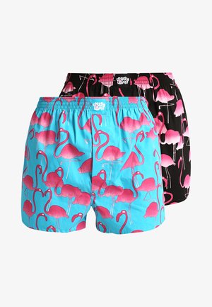 Zwei Paare Herren-Badeshorts: eines cyan mit pinken Flamingo-Mustern, das andere uni schwarz mit pinken Flamingos, beide mit elastischem Bund.